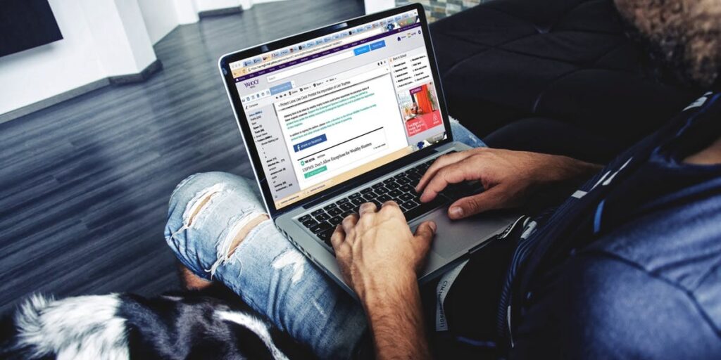 A man sits with a laptop in his lap looking at an email on his computer screen.