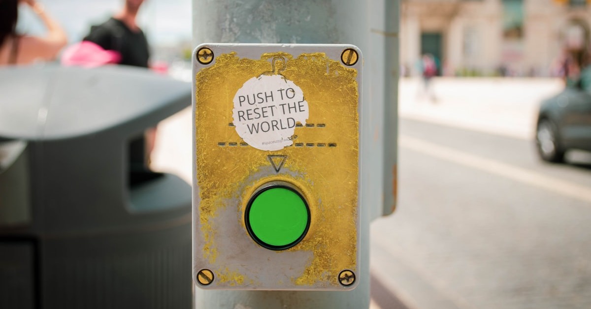 green button on street crossing post with a sticker that says "push to reset the world"