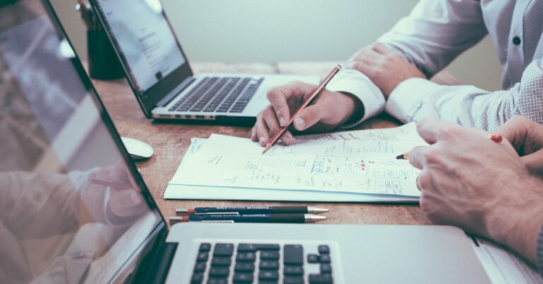 Two people working on laptops and drawing a diagram.