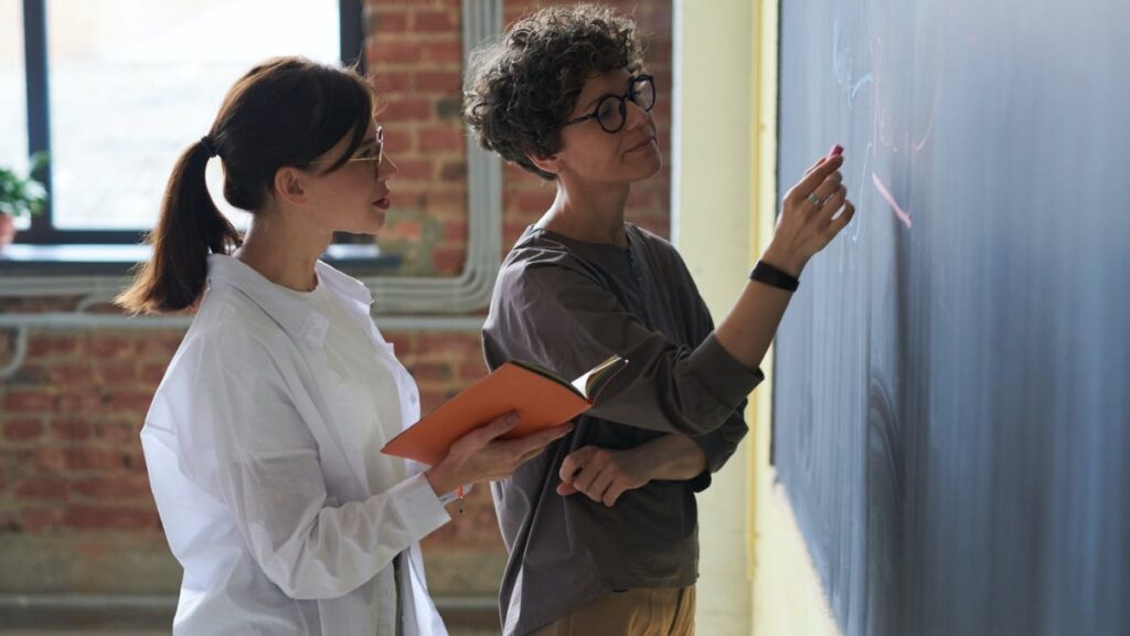 Two women examining a chalk board together.