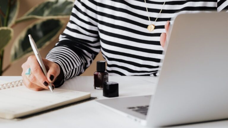 Woman in a black and white striped shirt taking notes in front of a computer.