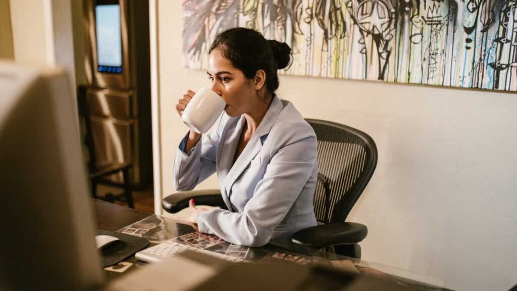 A woman at a desk drinking from a mug.
