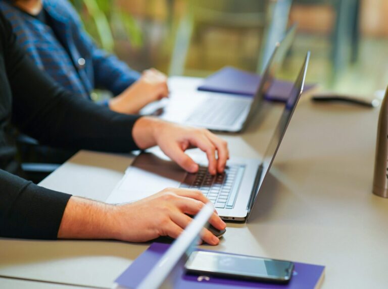 two people typing on laptops at a desk